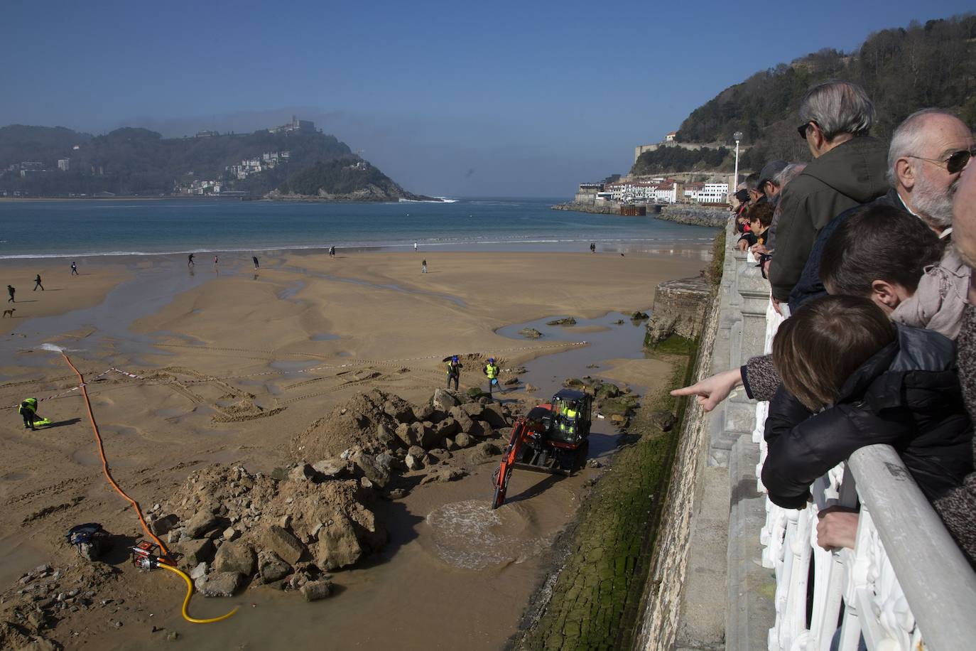 La playa de La Concha se ha convertido en la bajamar de este lunes por la mañana en un inesperado yacimiento arqueológico. La presencia de una pequeña excavadora retirando piedras y escombros junto al muro de costa a la altura del edificio consistorial ha suscitado una gran expectación entre los numerosos viandantes y turistas que han provechado el buen tiempo para dar un paseo. La máquina profundizaba en la arena en busca de los restos de un barco hundido del que hay constancia documental desde el siglo XVIII. 