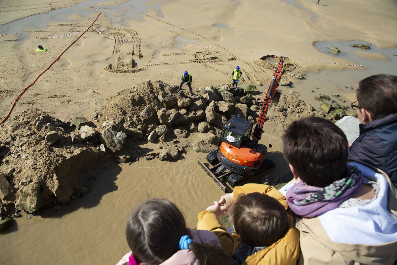 La playa de La Concha se ha convertido en la bajamar de este lunes por la mañana en un inesperado yacimiento arqueológico. La presencia de una pequeña excavadora retirando piedras y escombros junto al muro de costa a la altura del edificio consistorial ha suscitado una gran expectación entre los numerosos viandantes y turistas que han provechado el buen tiempo para dar un paseo. La máquina profundizaba en la arena en busca de los restos de un barco hundido del que hay constancia documental desde el siglo XVIII. 
