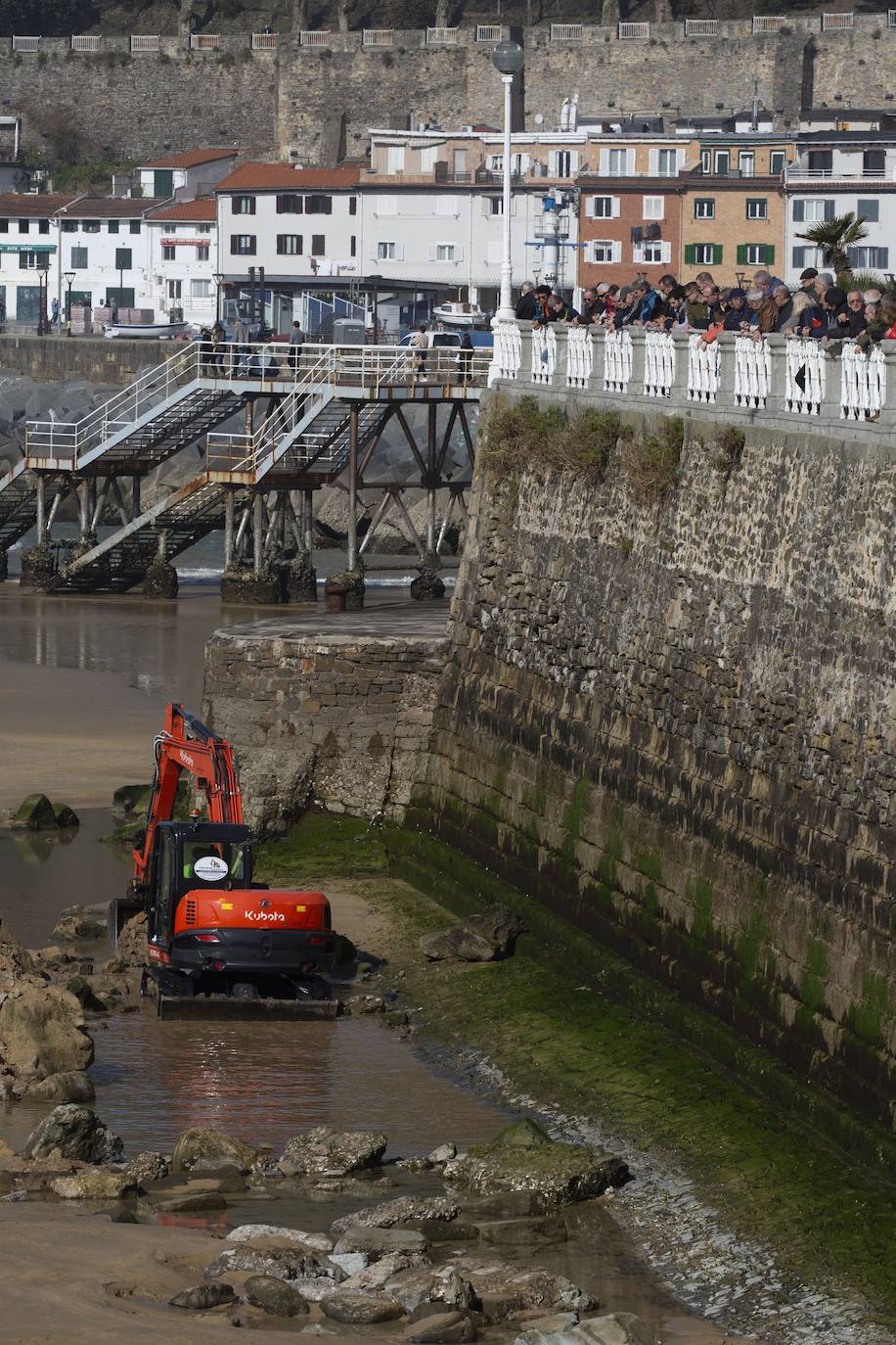 La playa de La Concha se ha convertido en la bajamar de este lunes por la mañana en un inesperado yacimiento arqueológico. La presencia de una pequeña excavadora retirando piedras y escombros junto al muro de costa a la altura del edificio consistorial ha suscitado una gran expectación entre los numerosos viandantes y turistas que han provechado el buen tiempo para dar un paseo. La máquina profundizaba en la arena en busca de los restos de un barco hundido del que hay constancia documental desde el siglo XVIII. 