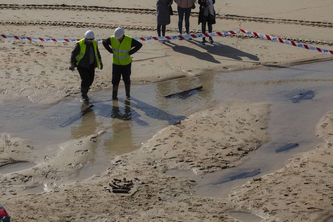 La playa de La Concha se ha convertido en la bajamar de este lunes por la mañana en un inesperado yacimiento arqueológico. La presencia de una pequeña excavadora retirando piedras y escombros junto al muro de costa a la altura del edificio consistorial ha suscitado una gran expectación entre los numerosos viandantes y turistas que han provechado el buen tiempo para dar un paseo. La máquina profundizaba en la arena en busca de los restos de un barco hundido del que hay constancia documental desde el siglo XVIII. 