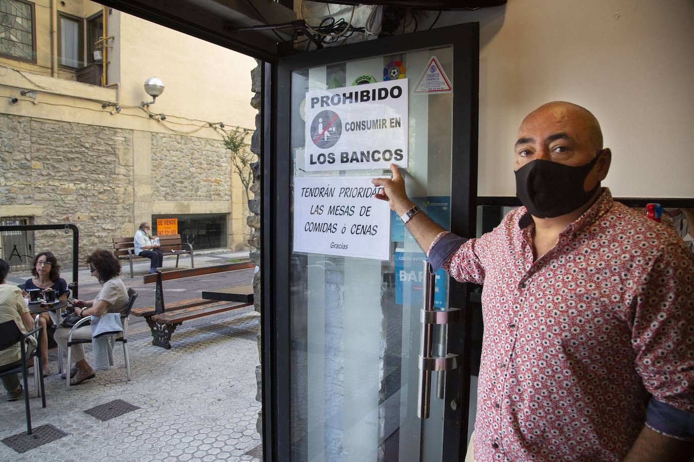 Aitor Garmendia señala el cartel en el que avisa de que los clientes del bar no pueden usar los bancos de la acera para sentarse. 