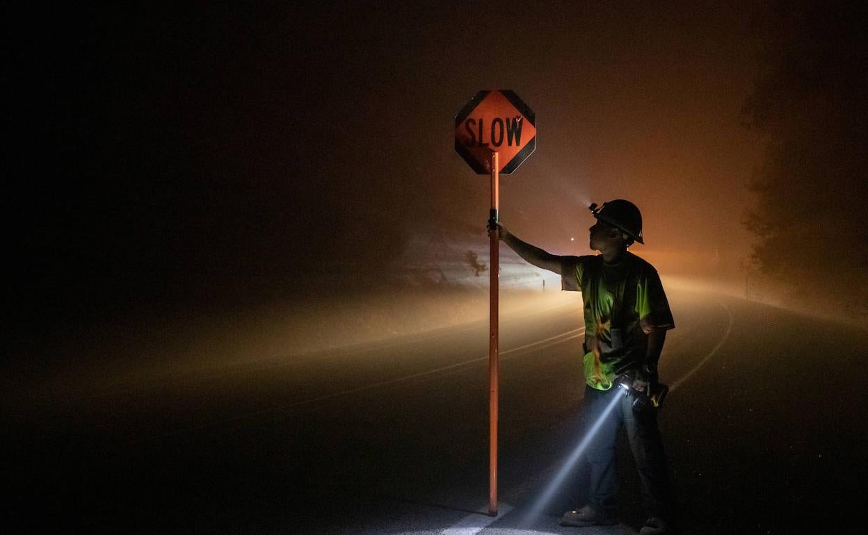 Un bombero sujeta un cartel pidiendo circular despacio por el humo de los incendios forestales en una carretera de Oregón.
