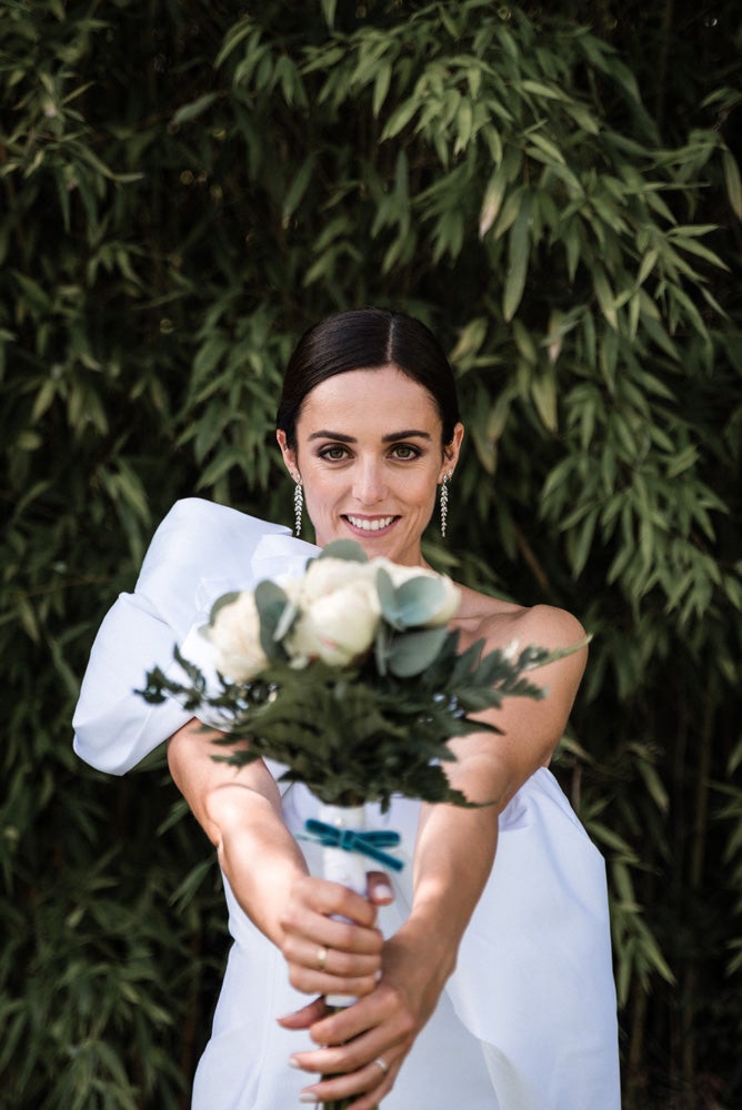 María y Jorge se casaron en Gorliz en una ceremonia íntima adaptada a las circunstancias. De largura 'mini' por encima de la rodilla, con corte asímetrico, volumen en la parte superior y lazadas laterales, la protagonista se ha convertido en una de las novias más impresionantes de las últimas semanas. El diseño lo ha firmado Fabio Encinar, uno de los diseñadores con sede en Madrid más de moda. En cuanto al peinado, otro de los elementos más destacados del estilismo, ha optado por un acertado moño bajo de bailarina súper pulido y tirante, con horquillas de Oui Novias