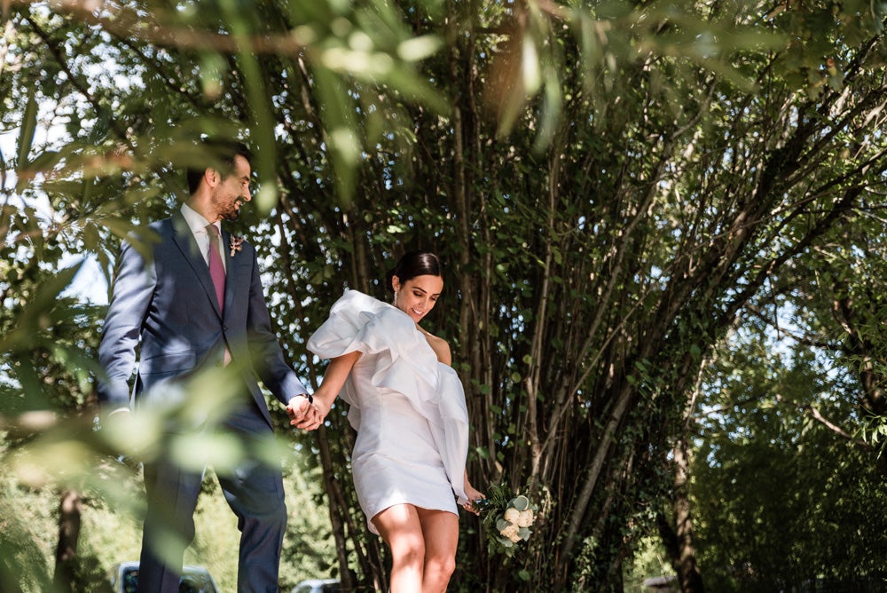 María y Jorge se casaron en Gorliz en una ceremonia íntima adaptada a las circunstancias. De largura 'mini' por encima de la rodilla, con corte asímetrico, volumen en la parte superior y lazadas laterales, la protagonista se ha convertido en una de las novias más impresionantes de las últimas semanas. El diseño lo ha firmado Fabio Encinar, uno de los diseñadores con sede en Madrid más de moda. En cuanto al peinado, otro de los elementos más destacados del estilismo, ha optado por un acertado moño bajo de bailarina súper pulido y tirante, con horquillas de Oui Novias