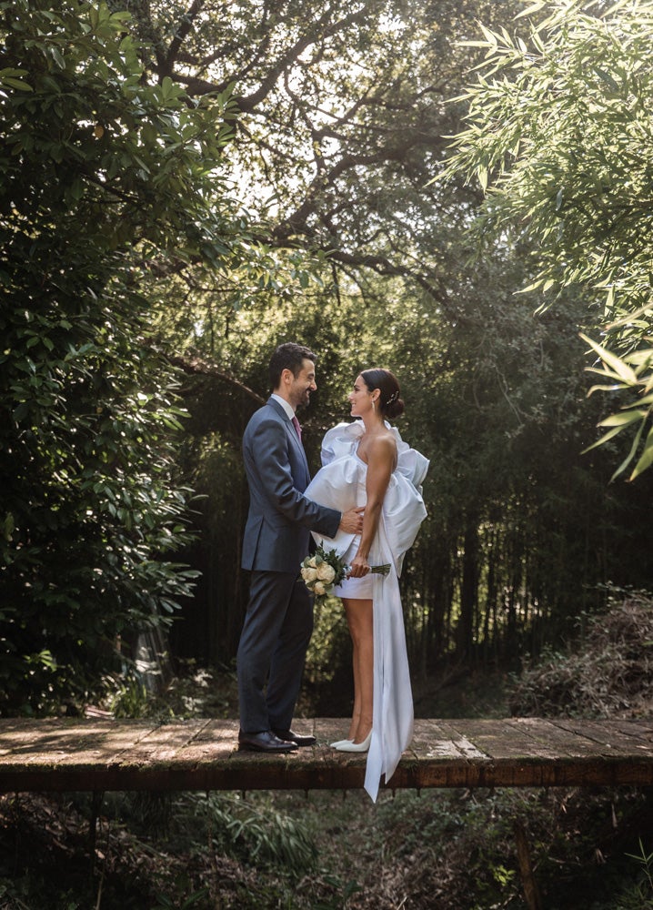 María y Jorge se casaron en Gorliz en una ceremonia íntima adaptada a las circunstancias. De largura 'mini' por encima de la rodilla, con corte asímetrico, volumen en la parte superior y lazadas laterales, la protagonista se ha convertido en una de las novias más impresionantes de las últimas semanas. El diseño lo ha firmado Fabio Encinar, uno de los diseñadores con sede en Madrid más de moda. En cuanto al peinado, otro de los elementos más destacados del estilismo, ha optado por un acertado moño bajo de bailarina súper pulido y tirante, con horquillas de Oui Novias