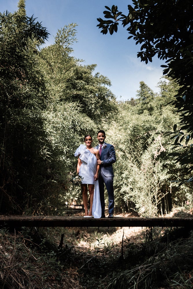 María y Jorge se casaron en Gorliz en una ceremonia íntima adaptada a las circunstancias. De largura 'mini' por encima de la rodilla, con corte asímetrico, volumen en la parte superior y lazadas laterales, la protagonista se ha convertido en una de las novias más impresionantes de las últimas semanas. El diseño lo ha firmado Fabio Encinar, uno de los diseñadores con sede en Madrid más de moda. En cuanto al peinado, otro de los elementos más destacados del estilismo, ha optado por un acertado moño bajo de bailarina súper pulido y tirante, con horquillas de Oui Novias