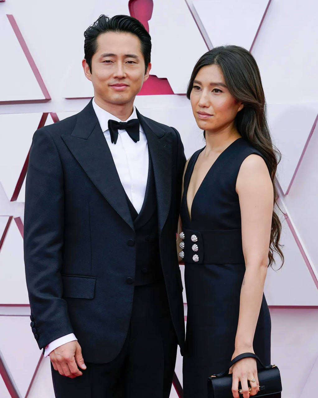 Joana Pak, acompañada de Steven Yeun, ha paseado una innata elegancia por la 'red carpet' de los Oscars, gracias a un favorecedor vestido 'minimal' en negro, con escote en V y un fajín con seis botones en color plata