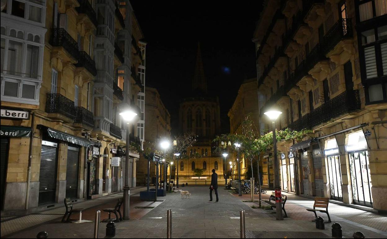 Una persona pasea su perro en la calle Reyes Católicos de Donostia, una vez iniciado el toque de queda.