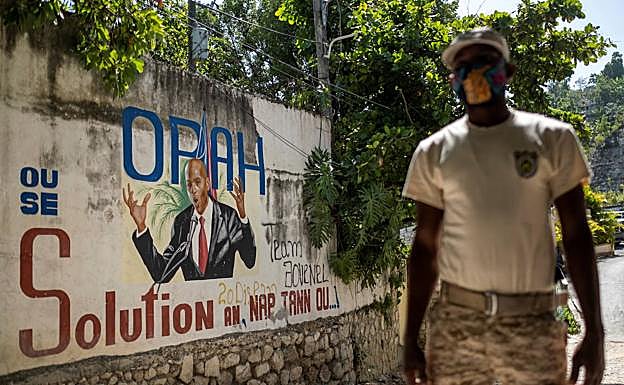 Un policía vigila una calle de Puerto Príncipe delante de una pintada alusiva al presidente Jovenel Moise.