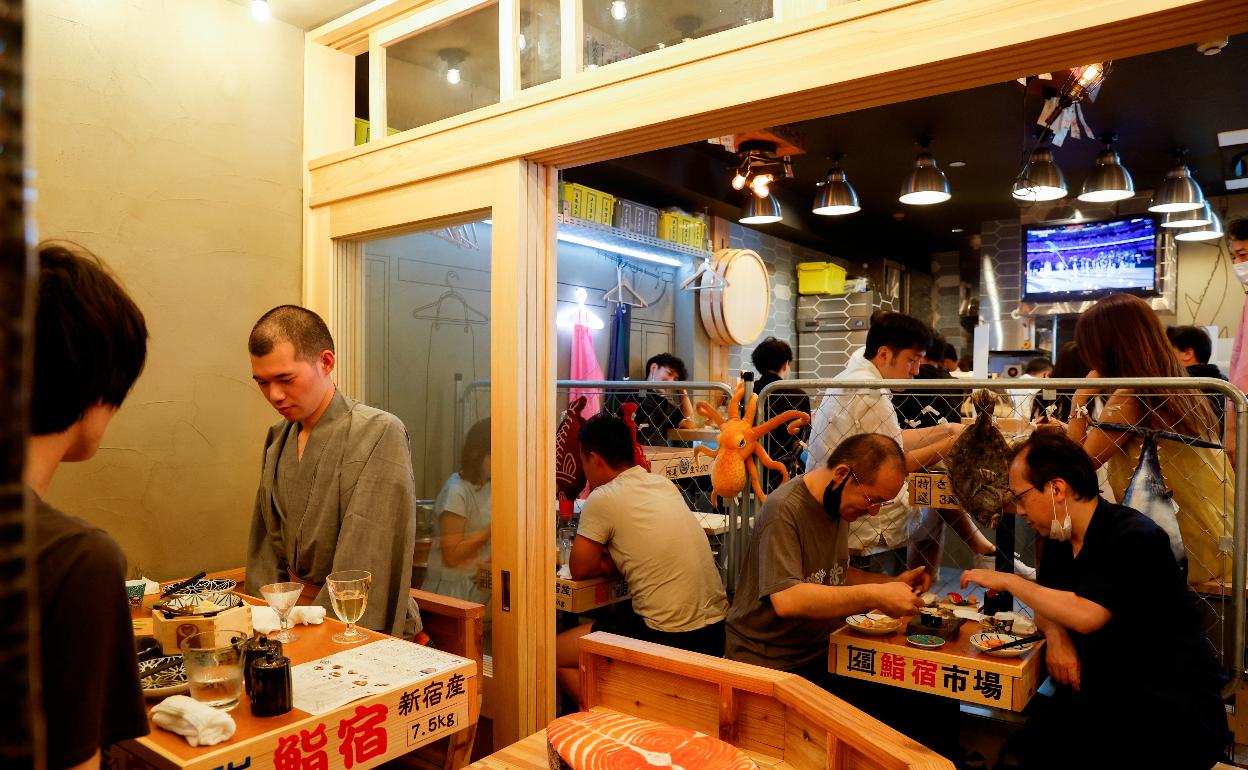 Los clientes de un bar en el barrio de Shinjuku de Tokio siguen por televisión la ceremonia. Comida y deporte. 