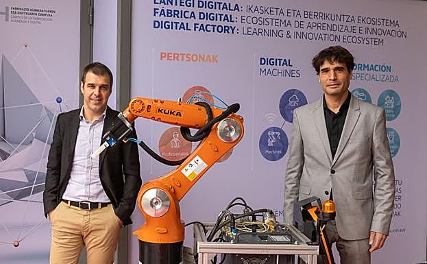 Ixaka Egurbide y Fernando Asenjo posan junto a un brazo robótico utilizado en el centro. 