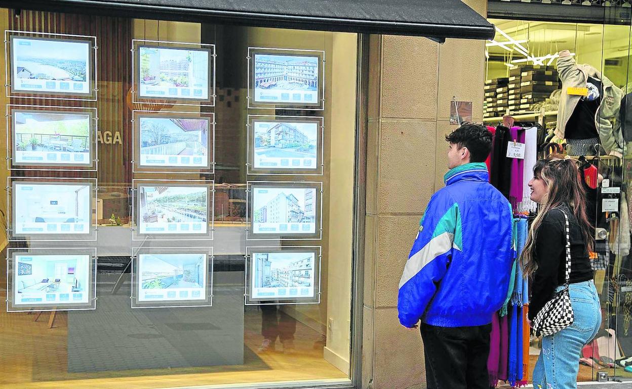 Dos jóvenes miran los anuncios de pisos en venta en el escaparate de una oficina inmobiliaria del Centro.