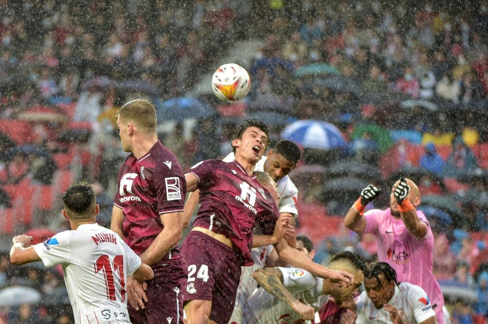 Sorloth y Le Normand saltan a rematar unbalón dentro del área sevillista en medio de un aguacero en el estadio Sánchez Pizjuán. 