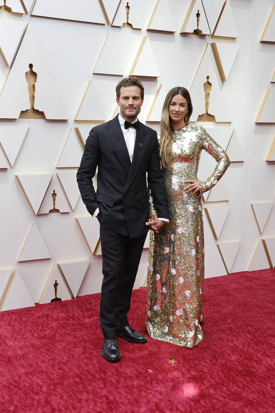 Jamie Dornan -conocido por el gran público como 'Grey'- ha elegido un elegante esmoquin negro de Valentino. Amelia Warner, su mujer, ha optado por un llamativo vestido de lentejuelas de Prada