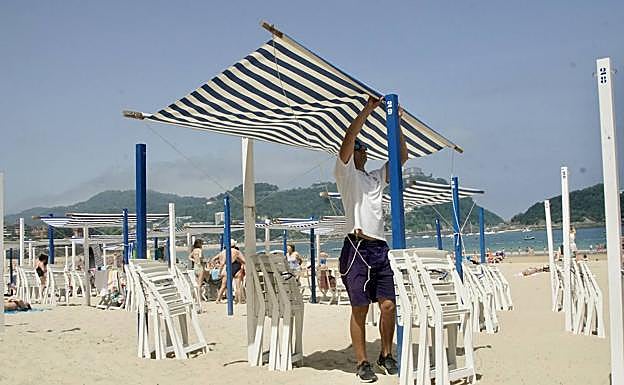 Un toldero se encarga de colocar uno de los parasoles en la playa de La Concha.