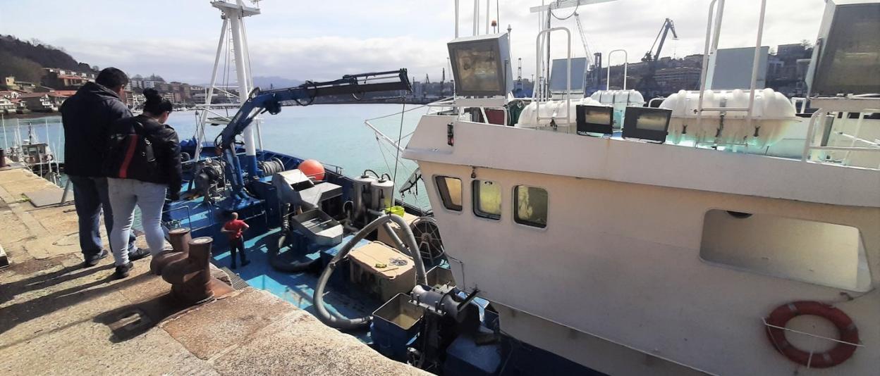 Dos personas contemplan cómo los arrantzales trabajan en la cubierta de su barco amarrado en el puerto de Pasaia. 