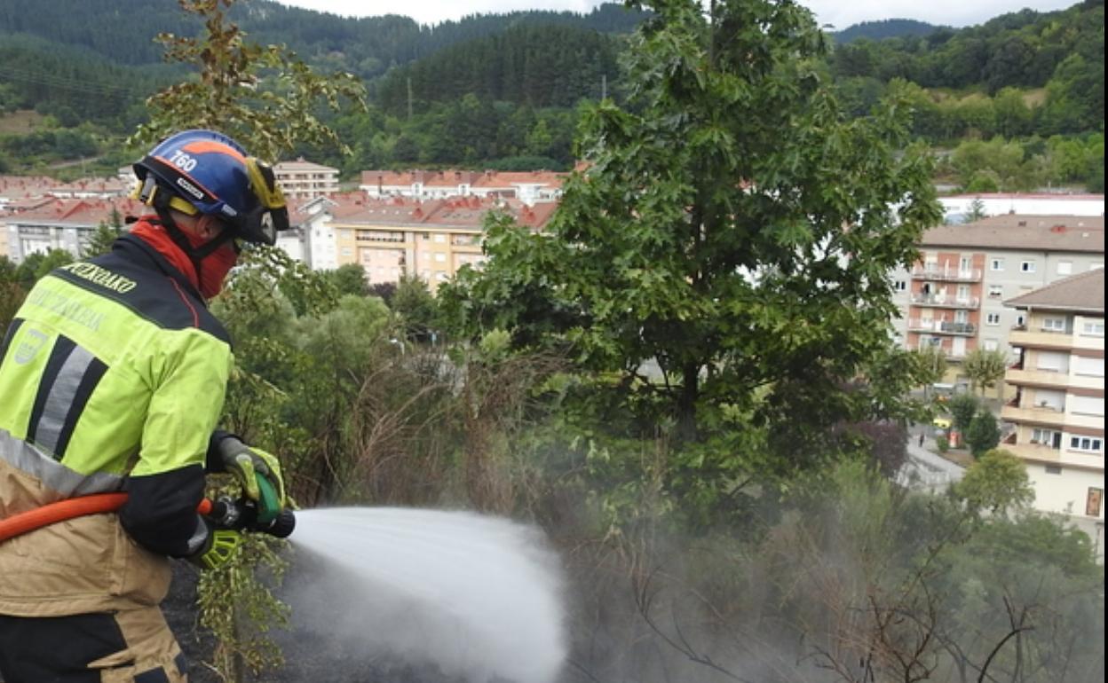 Fuego en la ladera del barrio de Txarapea, y bombero trabajando en la zona afectada. 