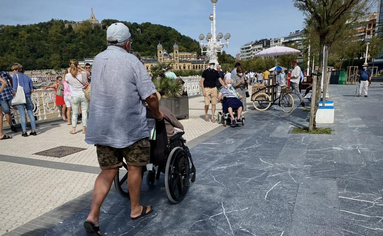 Dos mujeres en silla de ruedas, acompañadas por una persona, en el paseo de La Concha de Donostia.