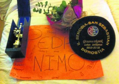 Imagen secundaria 1 - Arriba, Pedro Nimo en la Behobia de 2014, con la hermana de Arantza, fallecida en 2013. Abajo a la izquierda, cartulina de apoyo de unas jóvenes, trofeo, txapela y ramo de 2013. A la derecha, Nimo sube destacado el alto de Miracruz en 2013, cuando ganó.