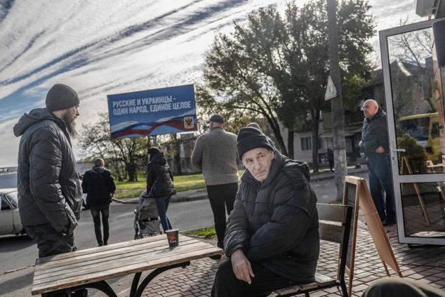 Un hombre bebe su café con un cartel publicitario ruso al fondo que reza 'Los rusos y los ucranianos son un pueblo, un todo', mientras la gente vuelve a su vida cotidiana en la recién liberada Jersón el 14 de noviembre de 2022