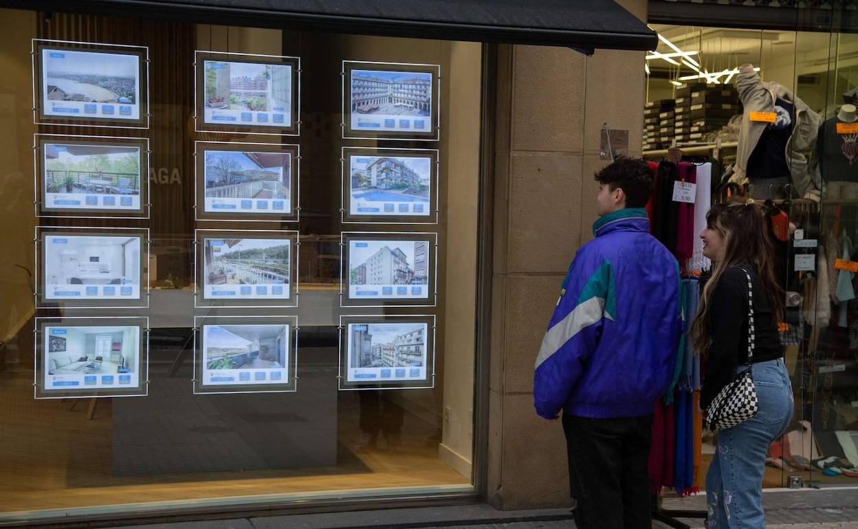 Dos jóvenes miran en un escaparate la oferta inmobiliaria. 