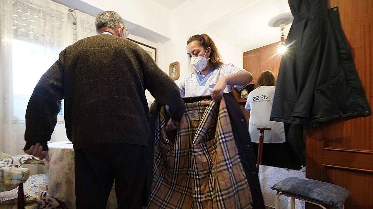 Una asistenta del hogar ayuda a un hombre a colocarse el abrigo.
