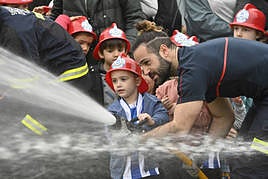 Un niño sujeta la manguera con la ayuda de un bombero de Donostia.