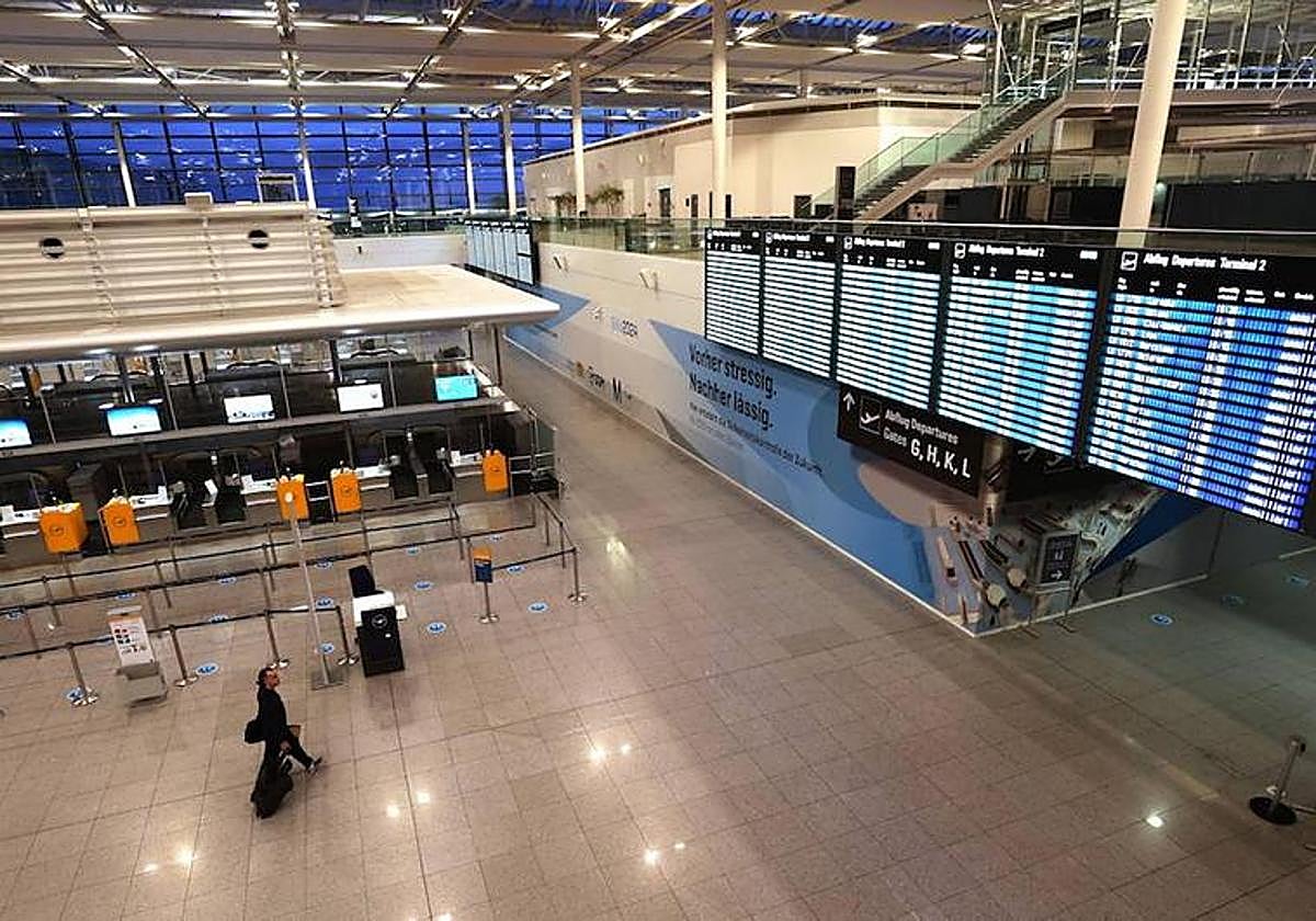 Un pasajero camina por la terminal desierta del aeropuerto de Munich y observa los paneles con todas las cancelaciones.