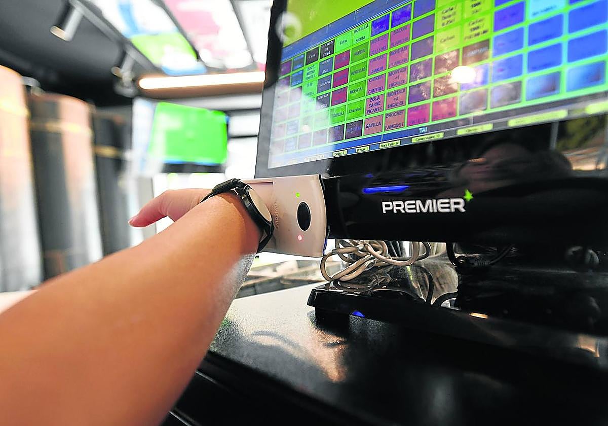 Un trabajador del bar Campus de San Sebastián ficha con su pulsera telemática en el ordenador del establecimiento.
