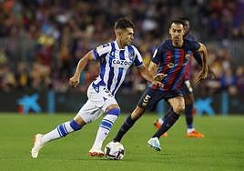 Martín Zubimendi avanza con el balón ante Sergi Busquets durante el Barcelona - Real Sociedad.