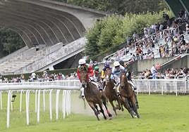 Los participantes en una carrera toman la curva frente a la tribuna del hipódromo.