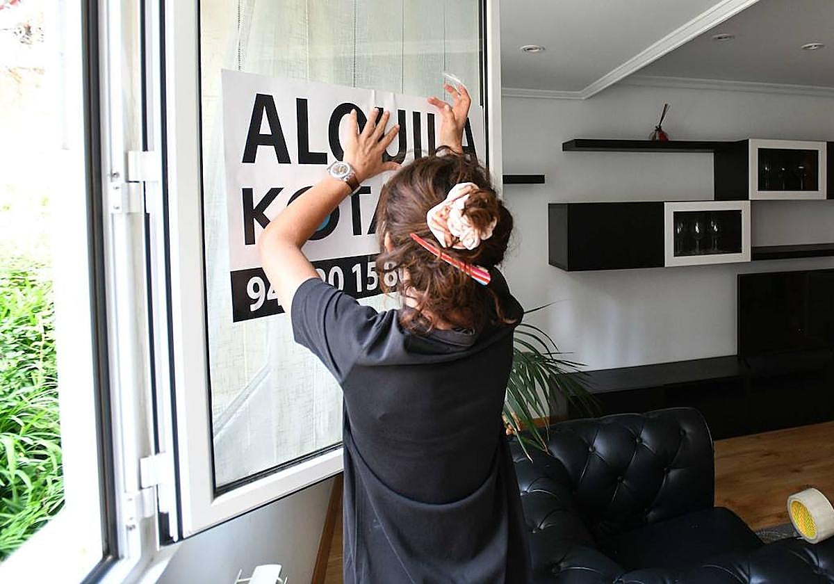 Una mujer coloca un cartel de alquiler en una vivienda de Eibar.