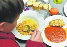 Un niño come unos garbanzos en un comedor escolar.