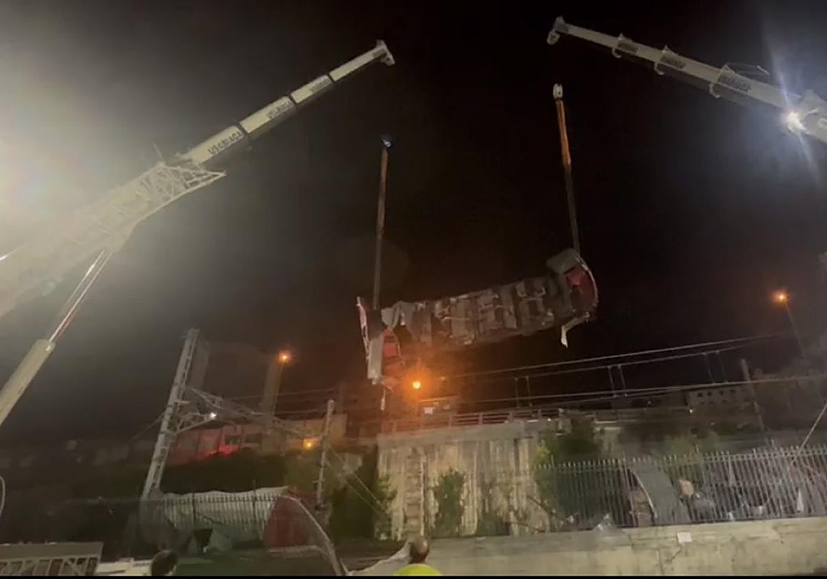 Uno de los vagones volcados en Pasaia es elevado por dos grandes grúas la madrugada de ayer.