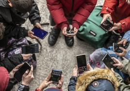 Varios adolescentes colocados en corro consultan las redes sociales en sus móviles.