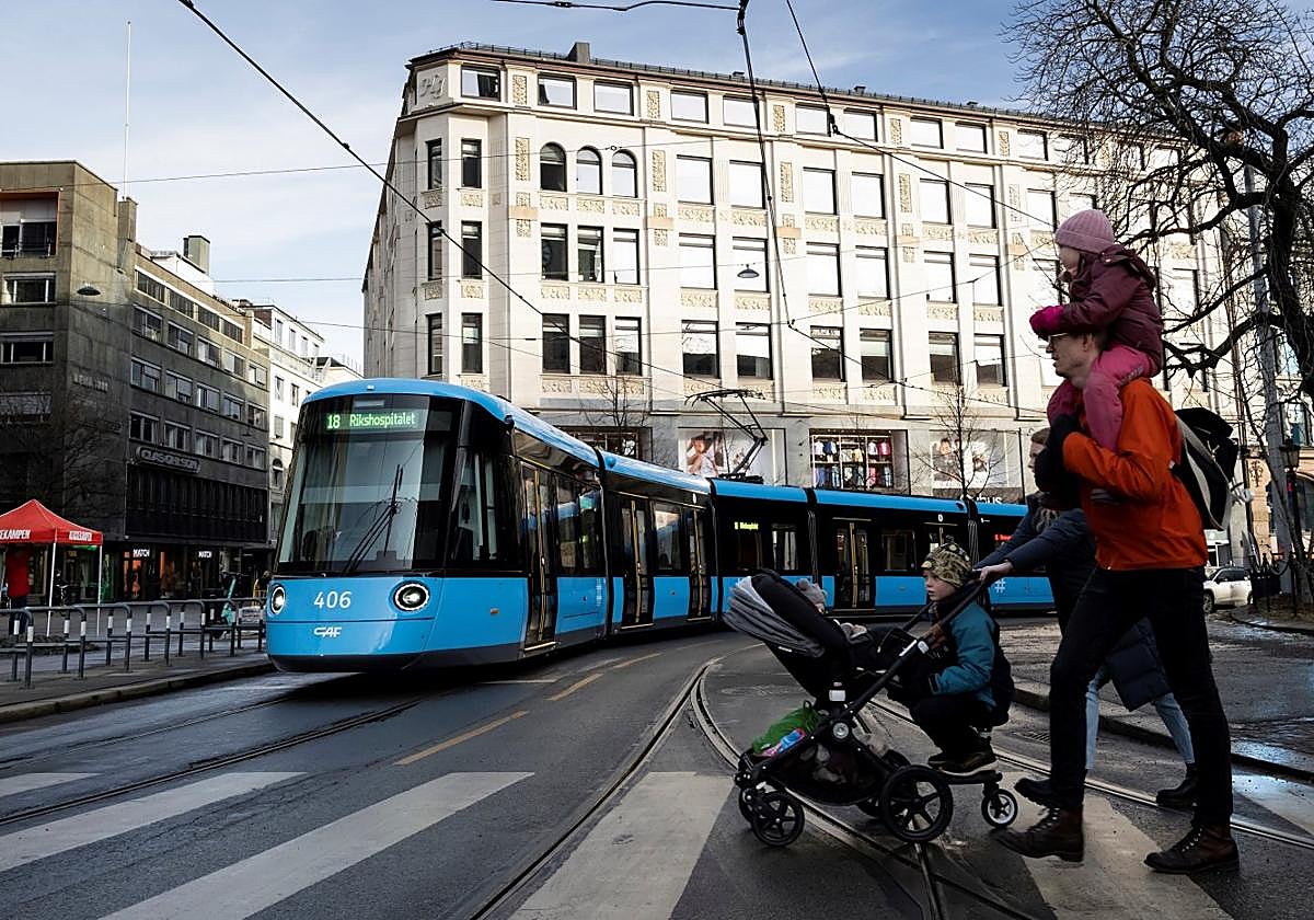Una familia se dispone a cruzar ante uno de los tranvías que CAF ha construido para el metro de la ciudad de Oslo.