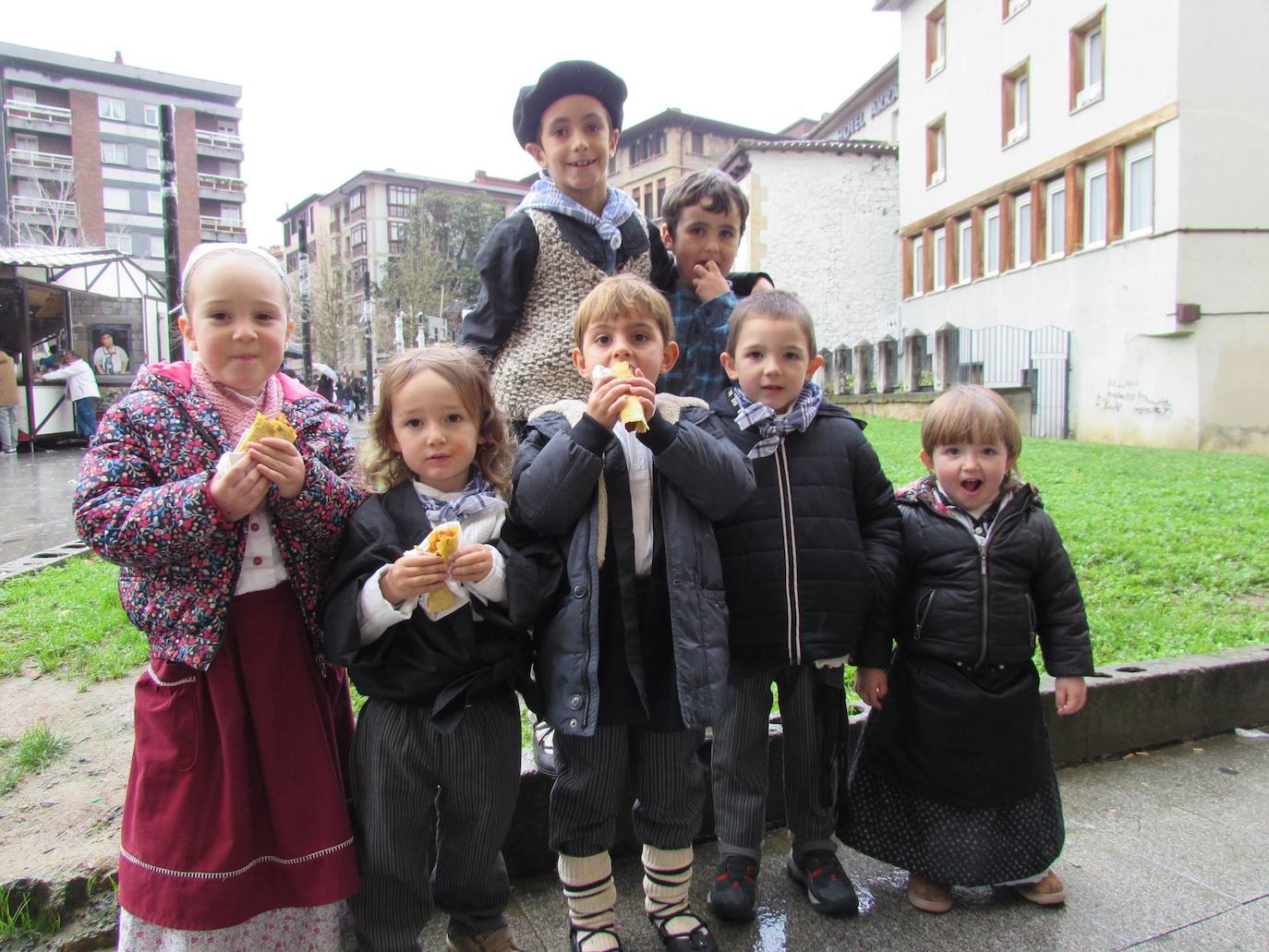 Imagen secundaria 2 - Arriba, una cuadrilla tomando un trago de sidra en la calle. Muchos consumidores realizaron sus compras navideñas en los puestos de alimentación instalados en la plaza Biteri. Debajo, niños comiendo talo con txistorra