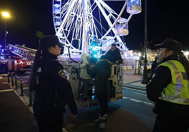 Los bomberos auxilian a uno de los niños rescatados de las cabinas ante la mirada de dos policías municipales.