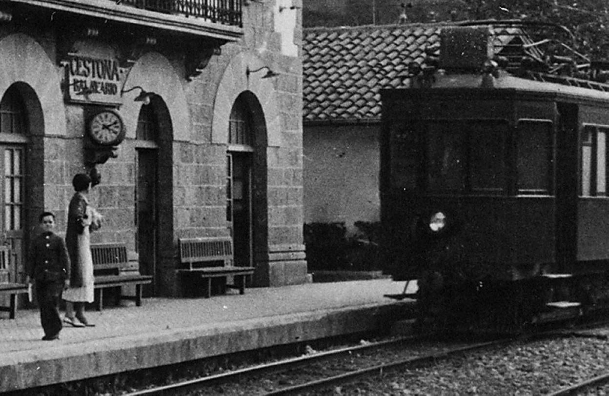 Antigua fotografía del tren del Urola llegando a la estación de Zestoa, donde se encuentran dos personas.