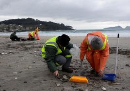 Dos personas recogen pélets en una de las playas de la localidad gallega de Nigrán.