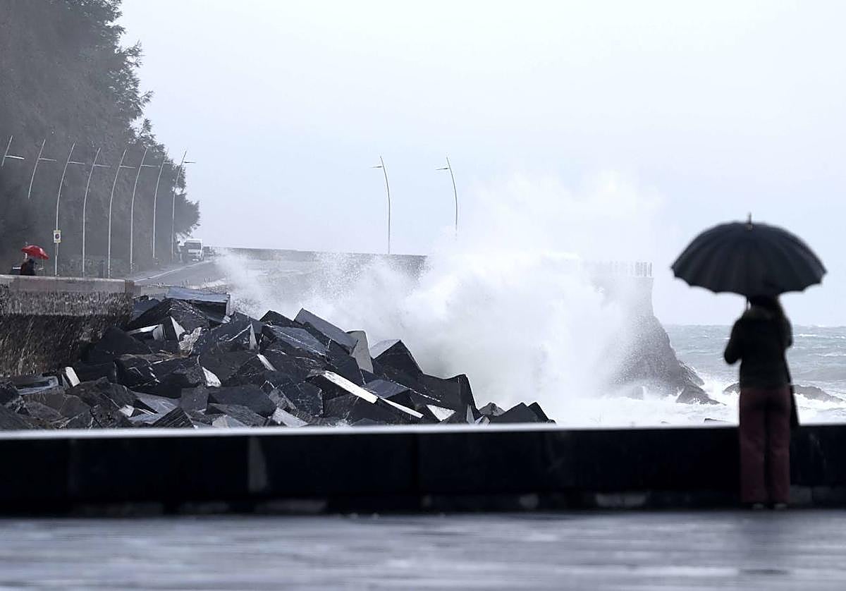 Una mujer con un paraguas observando el oleaje en el Paseo Nuevo de Donostia.