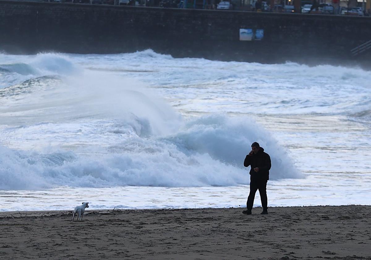 Un hombre pasea a su perro en la playa de Zurriola, en Donostia.