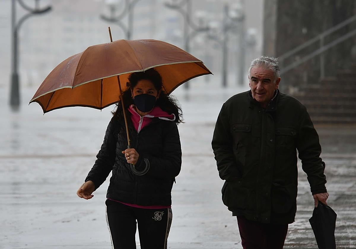 Dos personas pasean en Zarautz bajo la lluvia.