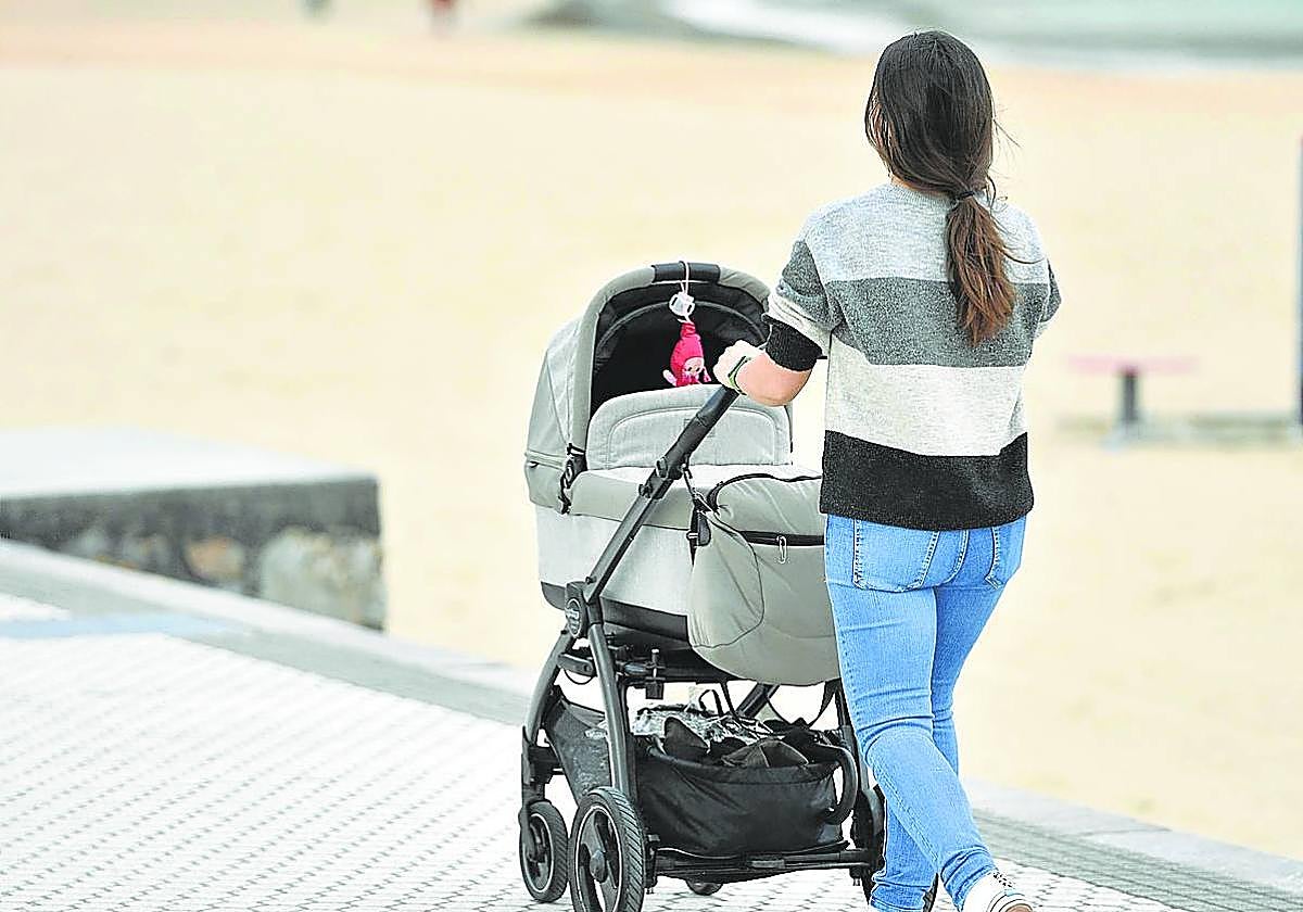 Una madre pasea a su bebé en un carrito junto a la playa de Ondarreta.