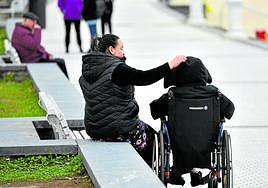 Una mujer cuida de una persona dependiente en silla de ruedas en el paseo de Ondarreta en San Sebastián.