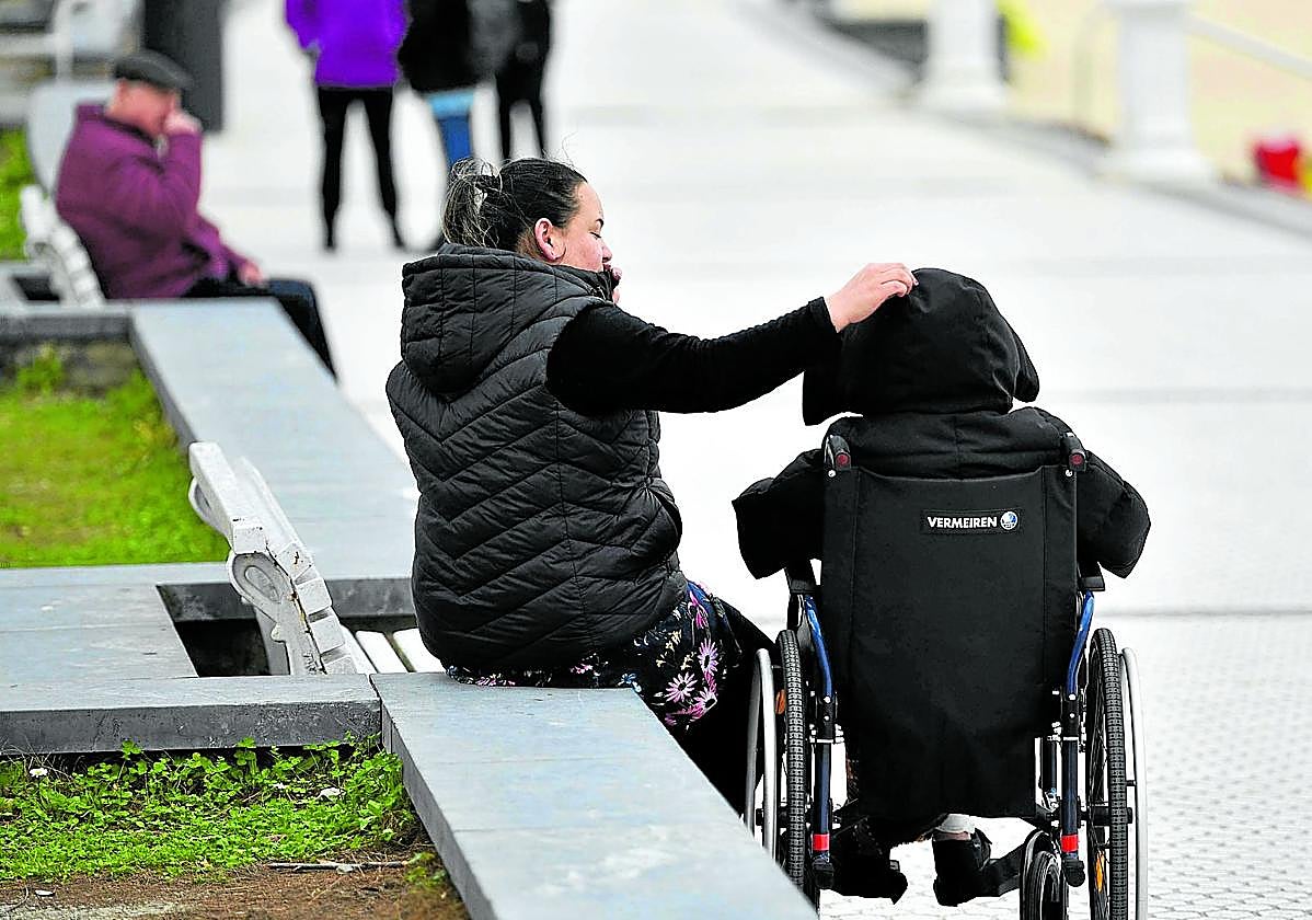 Una mujer cuida de una persona dependiente en silla de ruedas en el paseo de Ondarreta en San Sebastián.