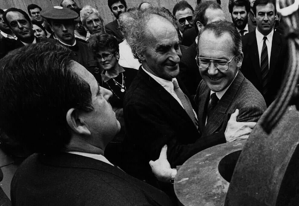 El escultor donostiarra Eduardo Chillida abarza a José Antonio Ardanza entre una multitud delante de una de sus esculturas.