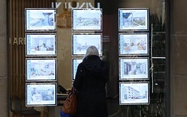 Una mujer protegida por un paraguas mira este martes las ofertas de alquiler en una inmobiliaria del centro de Donostia.