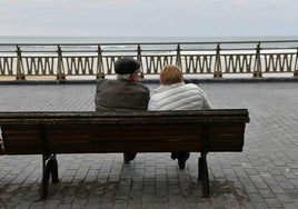 Dos personas mayores contemplan el mar sentadas en un banco.