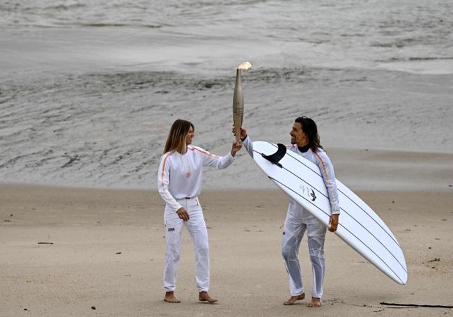 Los surfistas Zoe Grospiron y Edouard Delpero portan la antorcha olímpica en el relevo entre Biarritz y Anglet.